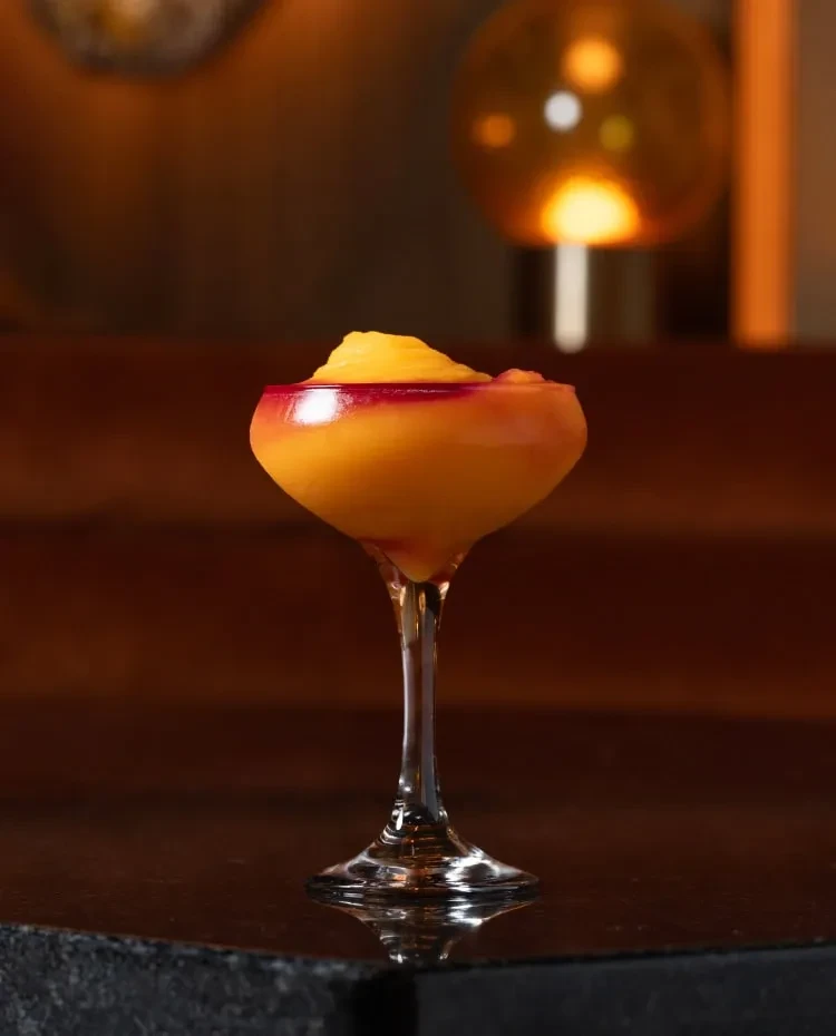 Vibrant yellow-orange and reddish-purple frozen cocktail in a coupe glass.
