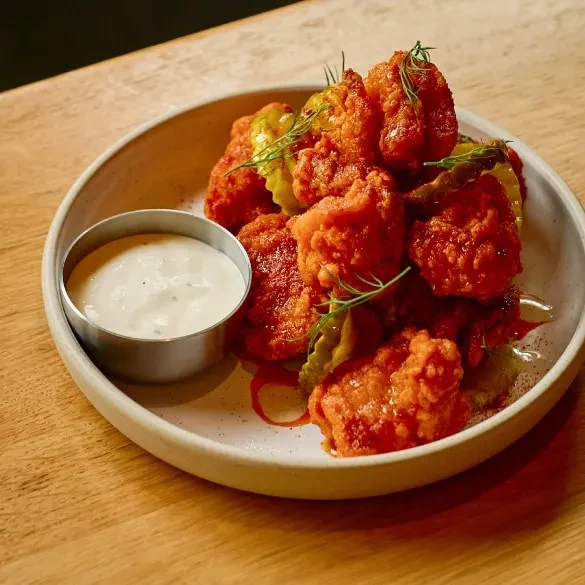 Crispy orange-red fried food with pickles and creamy dipping sauce.
