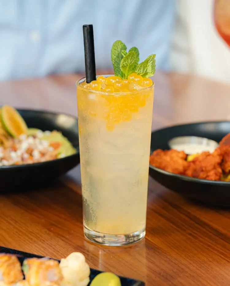 Frosted glass with yellow boba drink, mint garnish, and black straw.