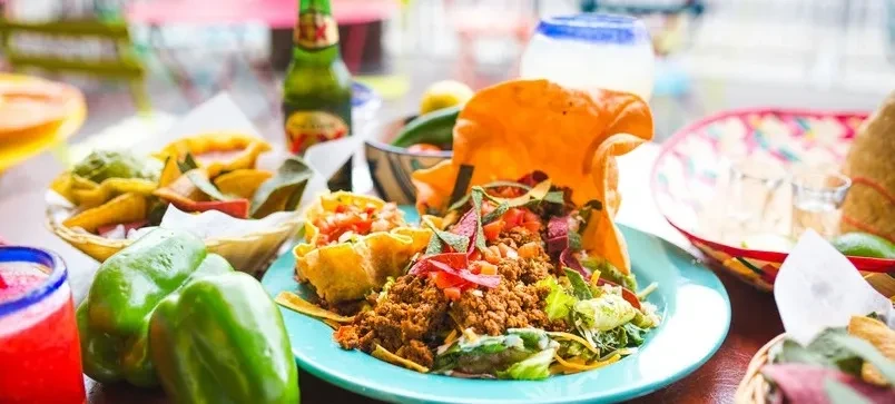Vibrant table with taco salad, chips, guacamole, and Mexican drinks.