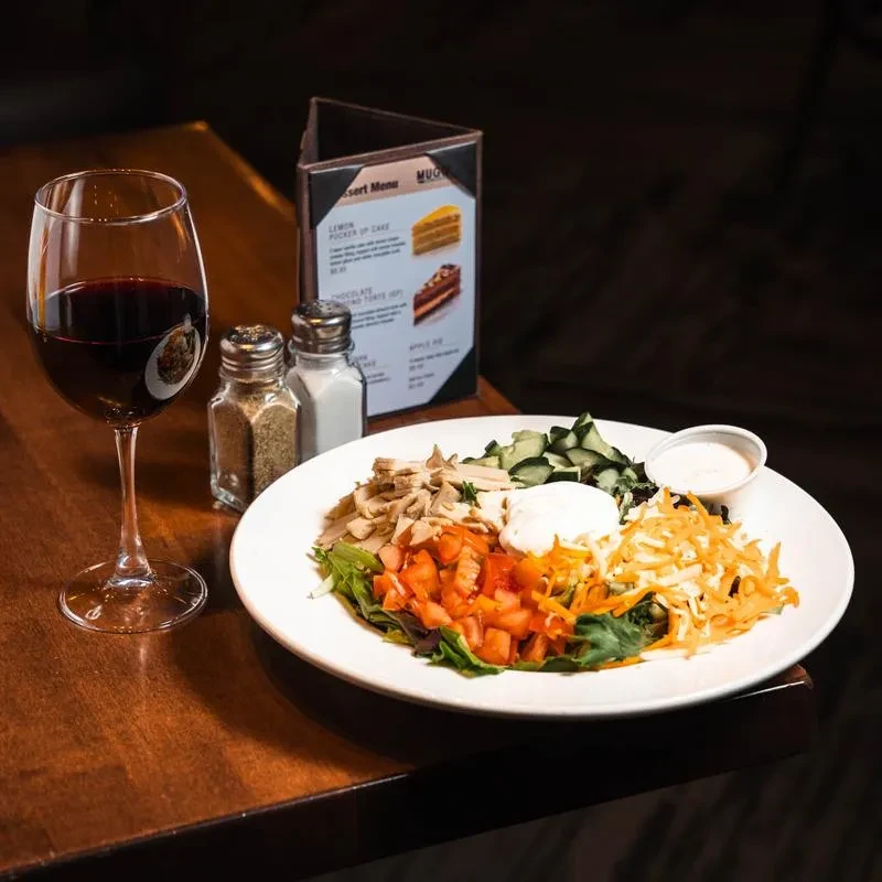 Plate of vibrant salad, red wine, and shakers on a wooden table.