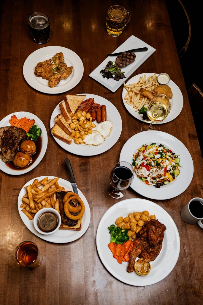 Table full of diverse pub food, drinks, seen from overhead perspective.