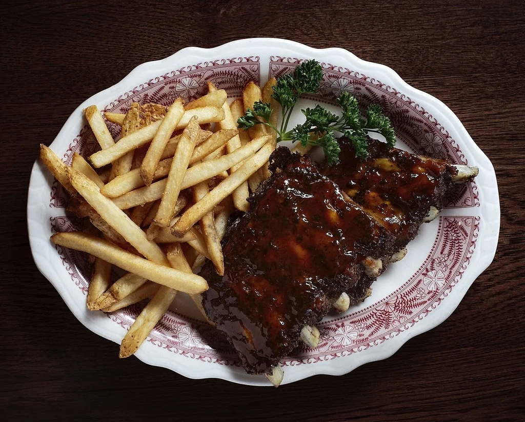 Saucy BBQ ribs, french fries, and parsley on a decorative plate, overhead.