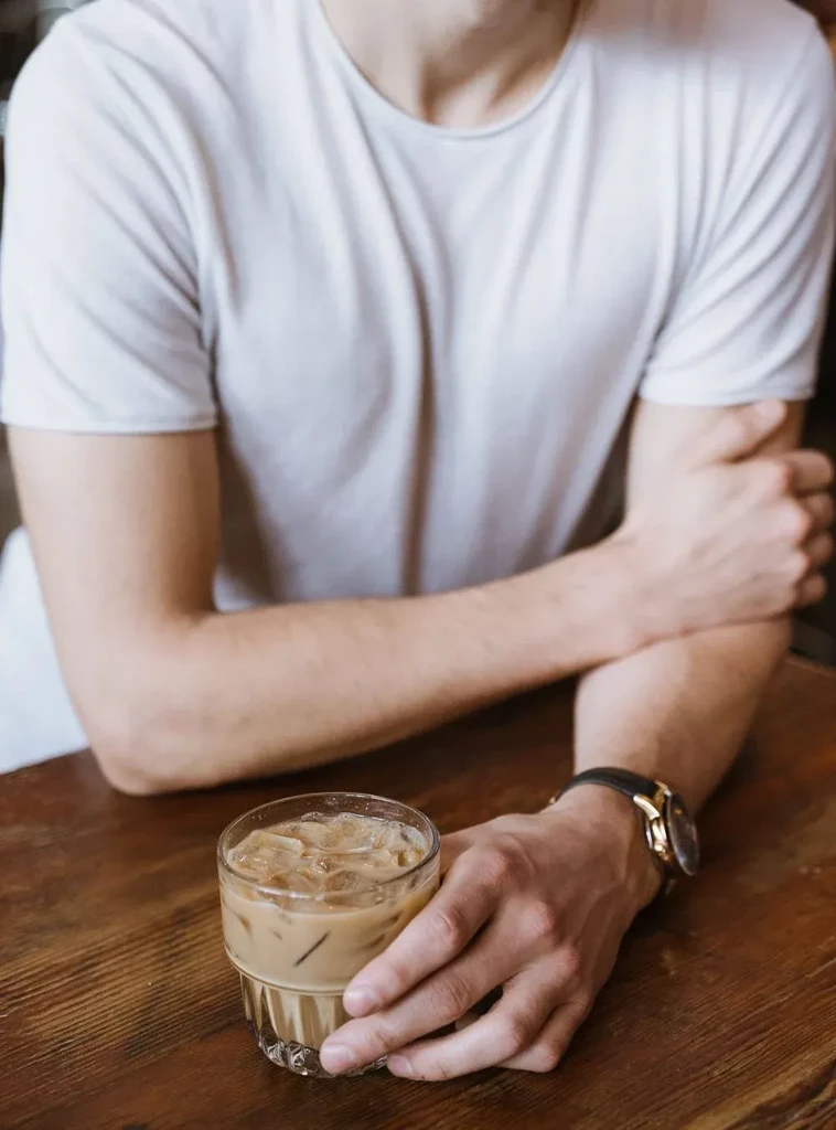 Close-up of person's arms holding iced coffee on a wooden table.