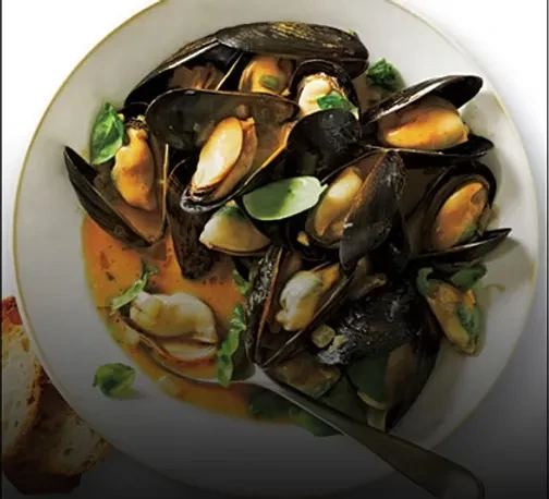 Cooked mussels with open shells, red broth, herbs, and crusty bread.