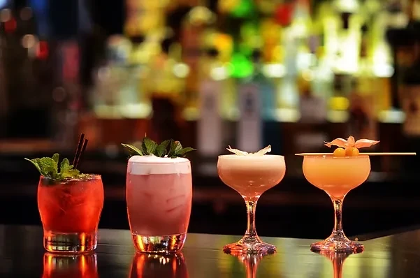 Four colorful, garnished cocktails on a reflective bar counter.