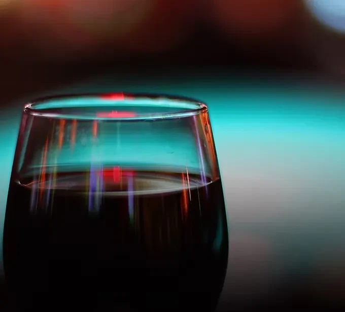 Dark drink in glass with vibrant red and blue light reflections.