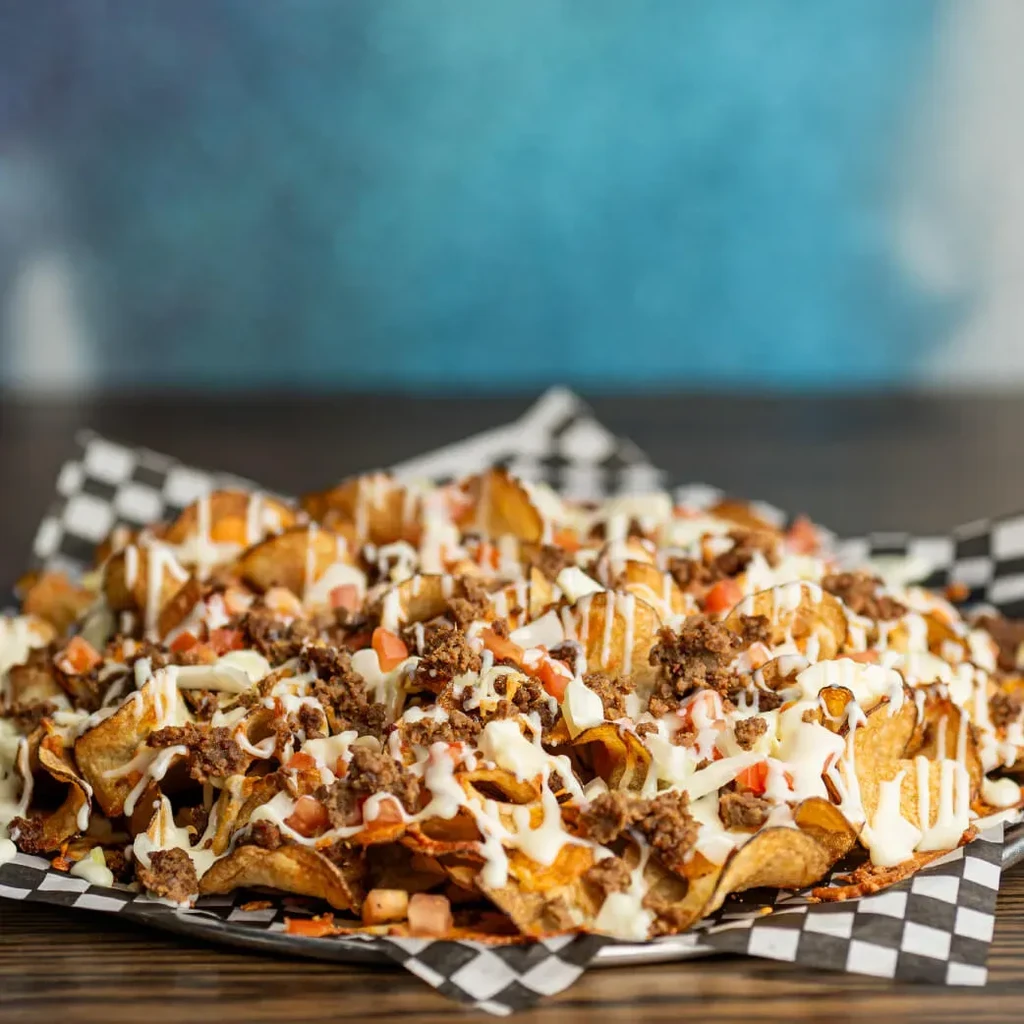Loaded potato chips topped with meat, cheese sauce, tomatoes, and diced white ingredients.