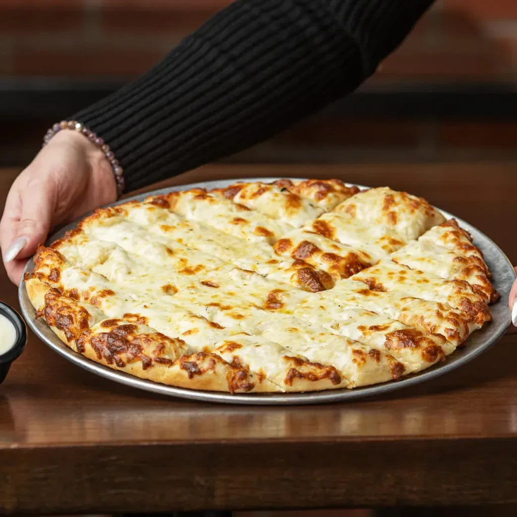 Hands holding silver pan with fresh, rectangular, cheesy flatbread slices.