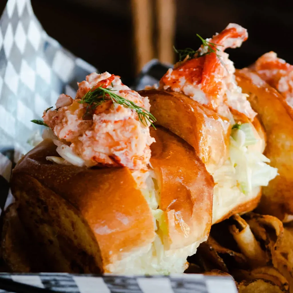Close-up of two golden-brown lobster rolls with dill and chips.