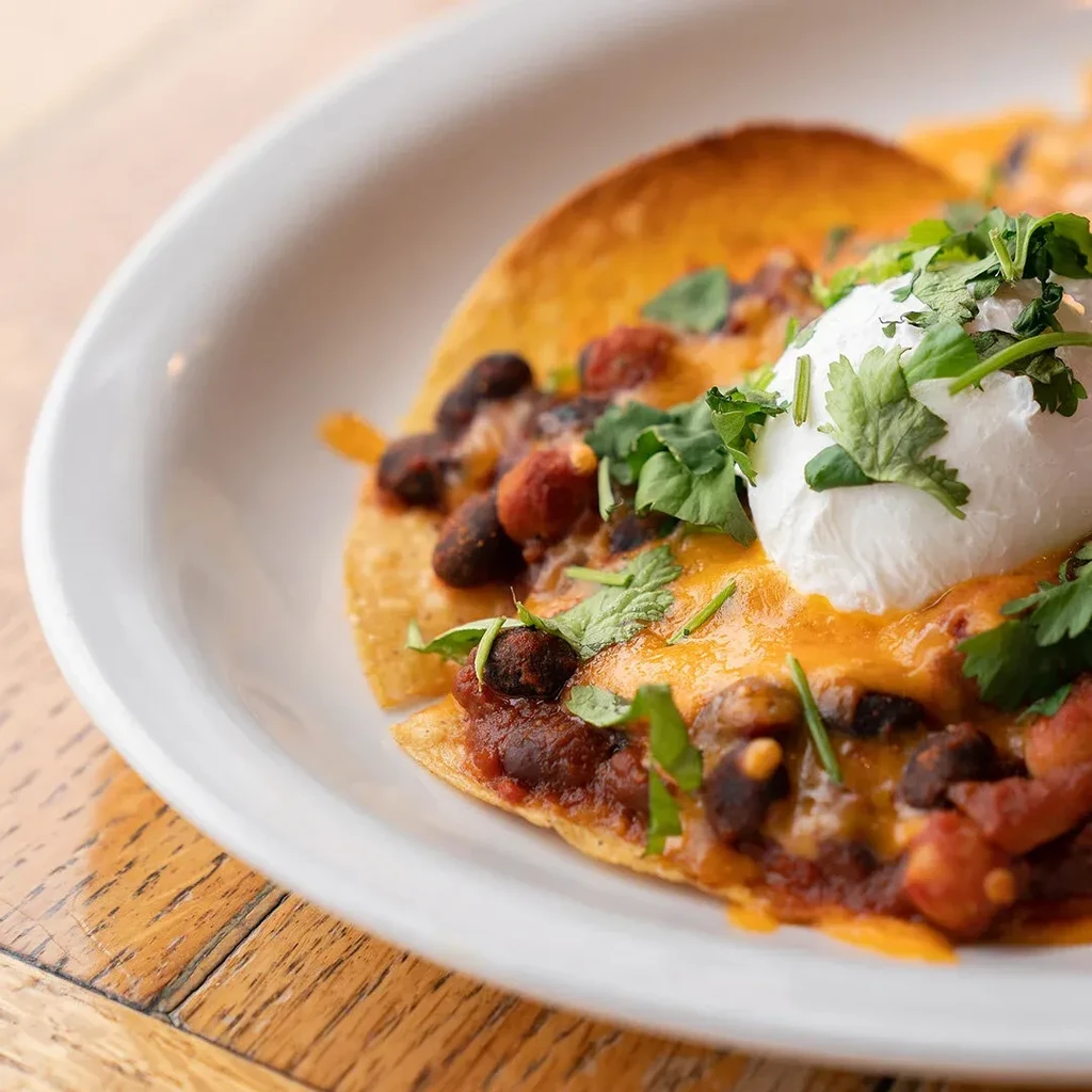 Loaded tostada with melted cheese, black beans, sauce, crema, cilantro.