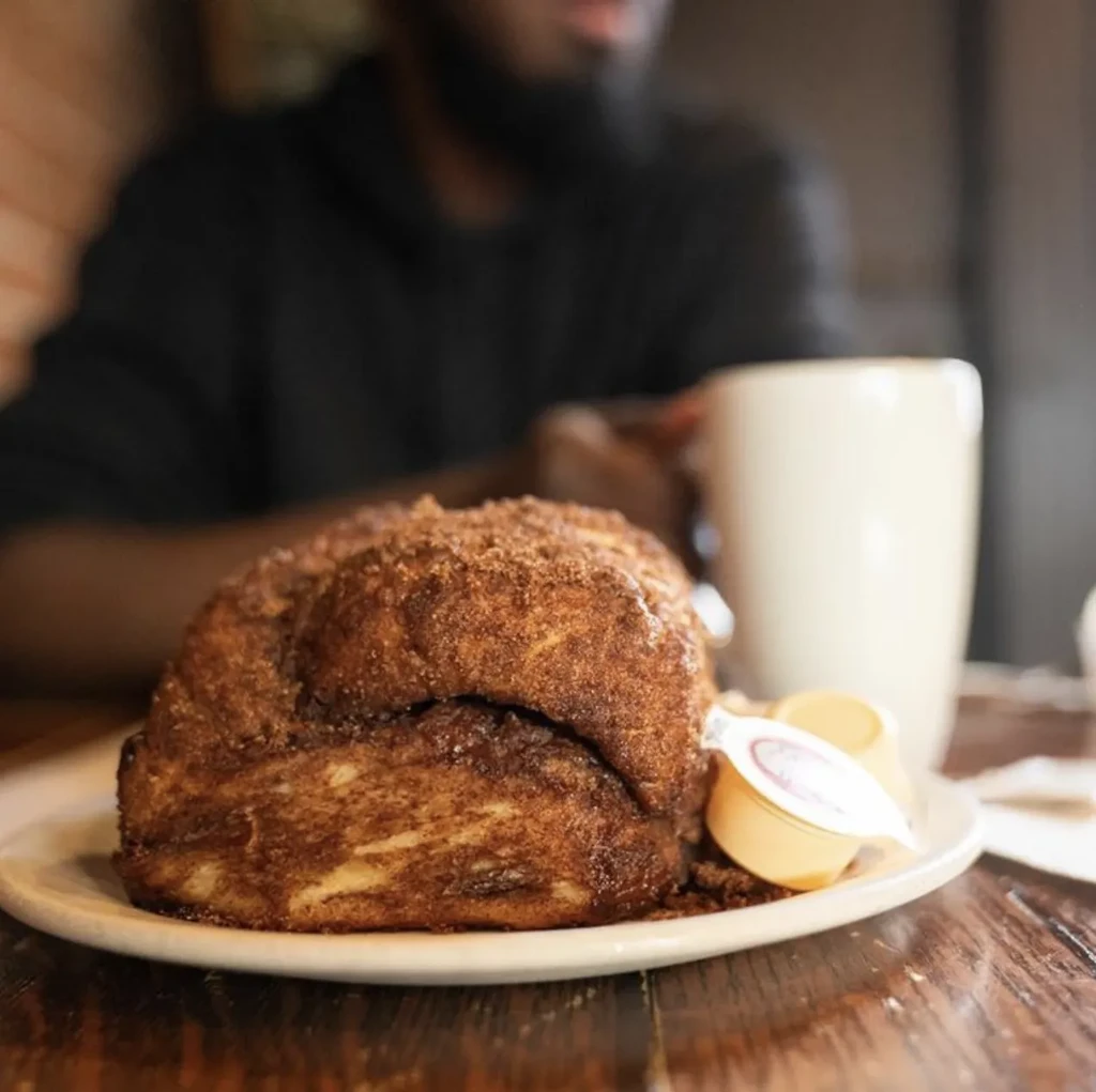 Golden-brown cinnamon bread dusted with sugar, creamers, blurred person.
