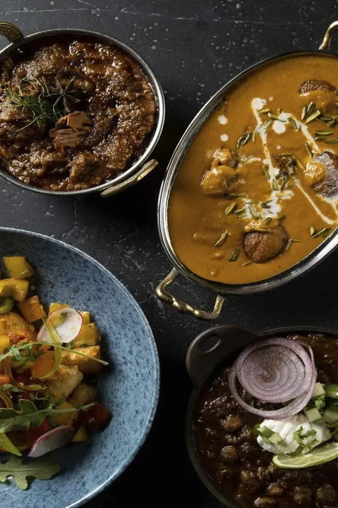 Four distinct curries and a colorful salad on a dark surface.