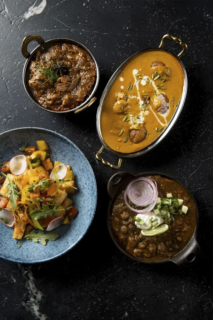 Four distinct food dishes: curries, salad, and lentil dish on dark stone.