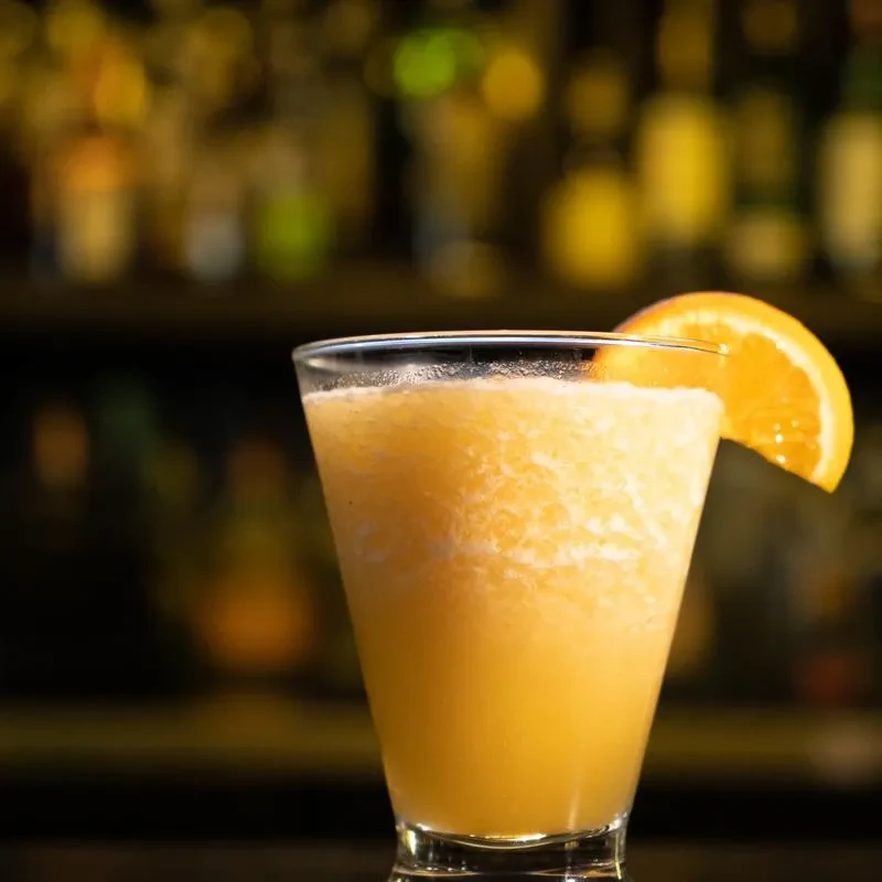 Blended orange drink with a slice in a dim bar setting.