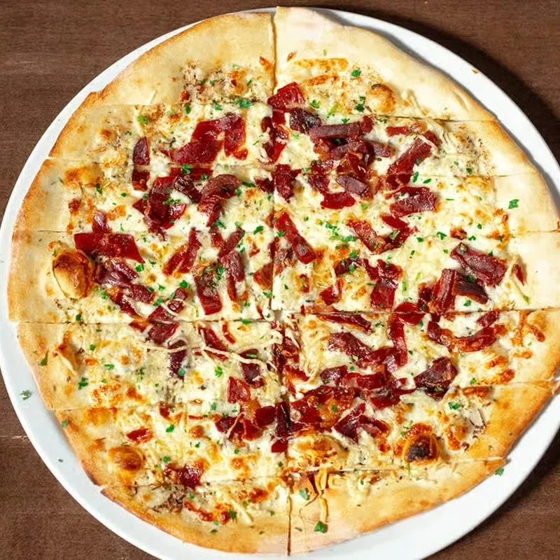 Top-down pizza with white cheese, crispy meat, and green herbs.