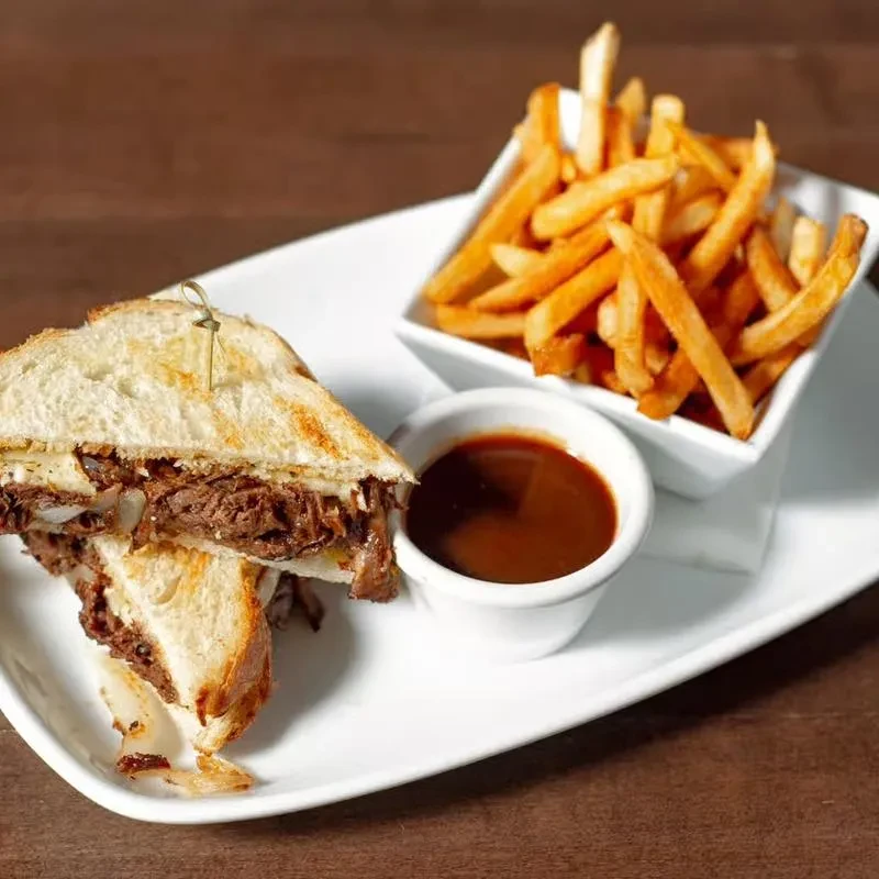 Close-up of a shredded beef sandwich, fries, and dipping sauce.