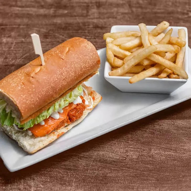 Top-down view of a buffalo chicken sub with fries on a white plate.