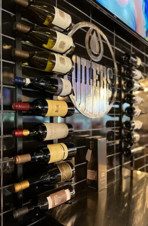 Wall-mounted wine rack with diverse bottles beside an Oilers sign.