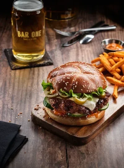 Close-up of burger, fries, sauce, and beer on a wooden table.
