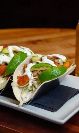 Two tacos with crispy fried filling, avocado, salsa, and lime.