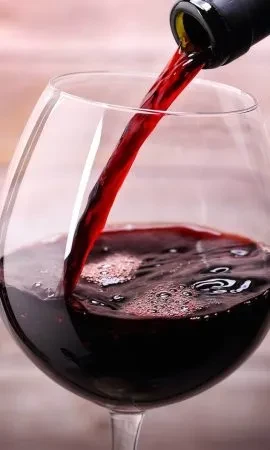 Close-up of red wine pouring from a bottle into a clear glass.