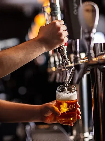 Hands pour golden beer from a tap into a glass at a bar.