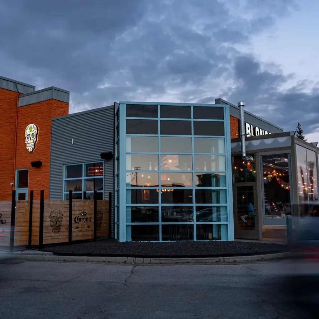 Modern restaurant with a neon sugar skull sign at dusk.