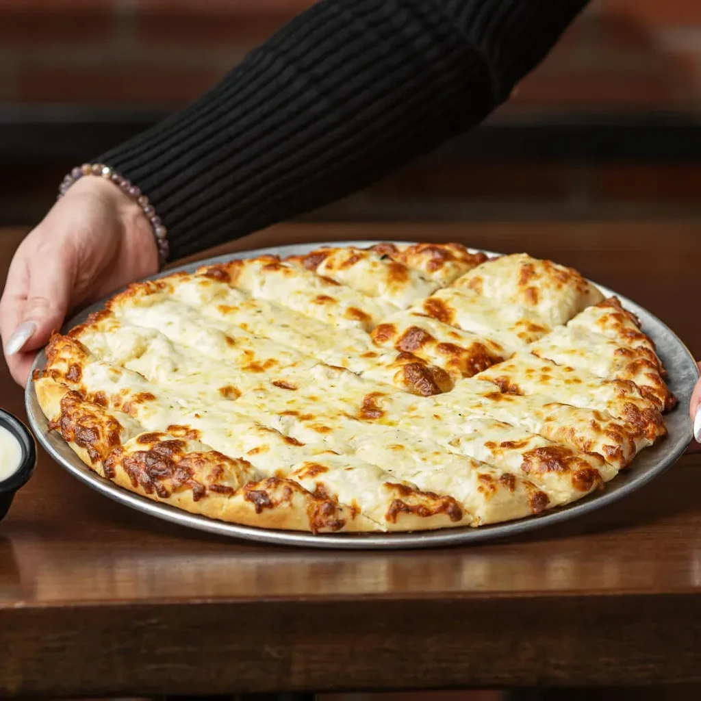 Hands hold a platter of freshly baked, bubbly cheesy breadsticks.