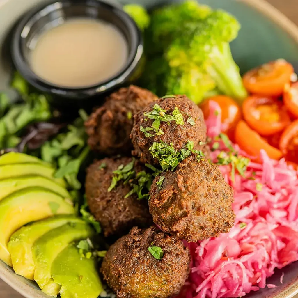Vibrant falafel bowl with avocado, broccoli, tomatoes, pickled red cabbage.