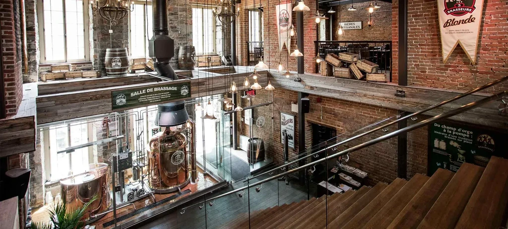 Multi-level brewpub with copper brewing tanks, wooden barrels, and exposed brick.