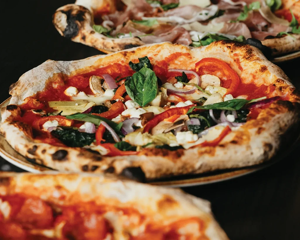Wood-fired vegetarian pizza in focus, with two other pizzas blurred.