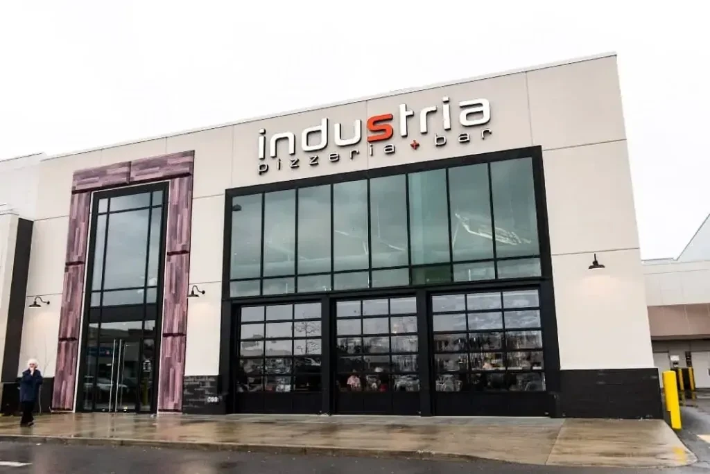 Modern Industria Pizzeria + Bar exterior with glass panels on a wet day.