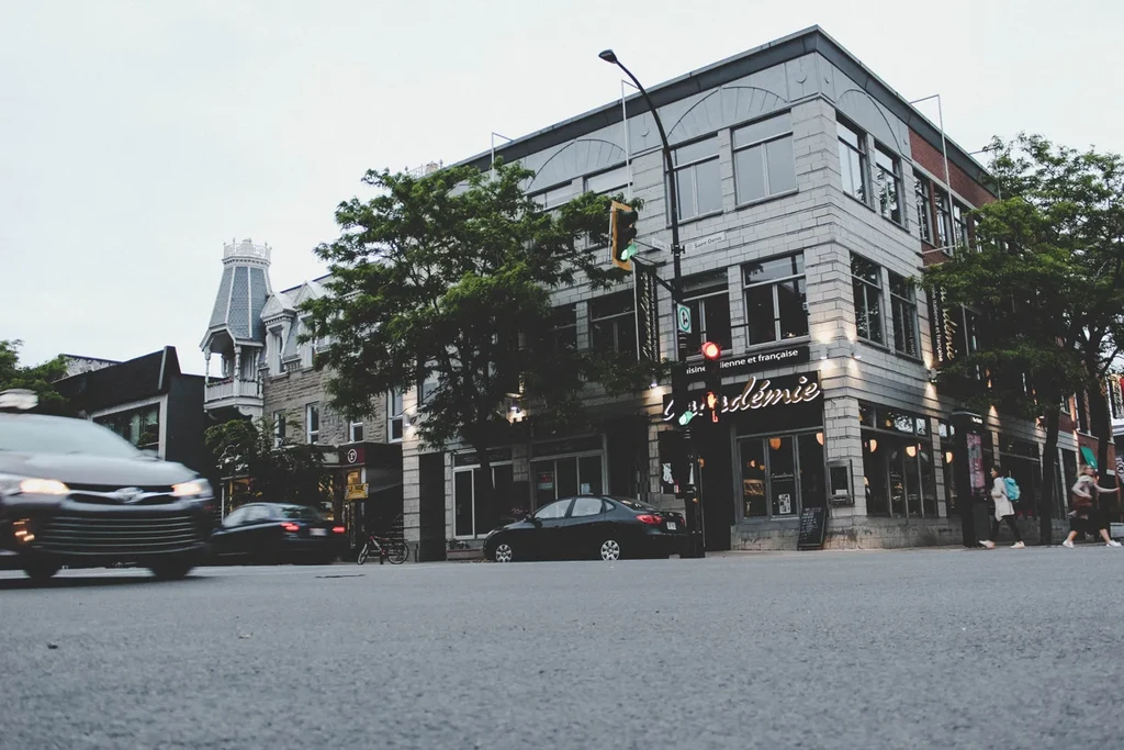 Overcast urban street scene featuring L'Académie restaurant and a turreted building.