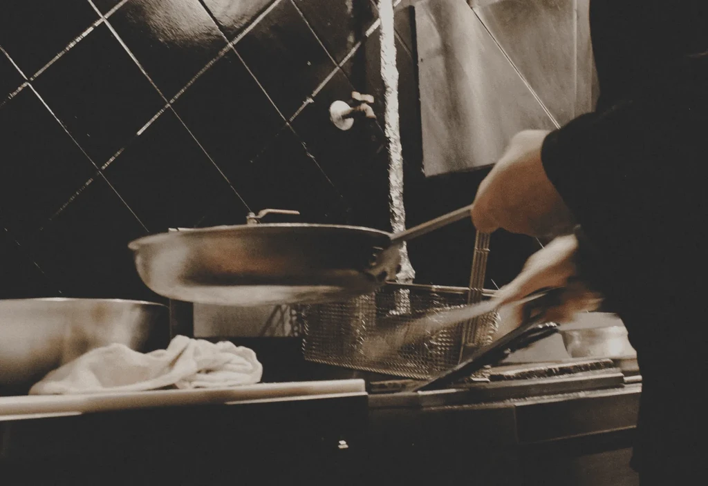 Motion-blurred hands tossing food in a dim, sepia-toned kitchen.