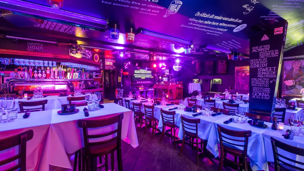 Empty restaurant interior with purple-blue lighting, bar, set tables, stage.