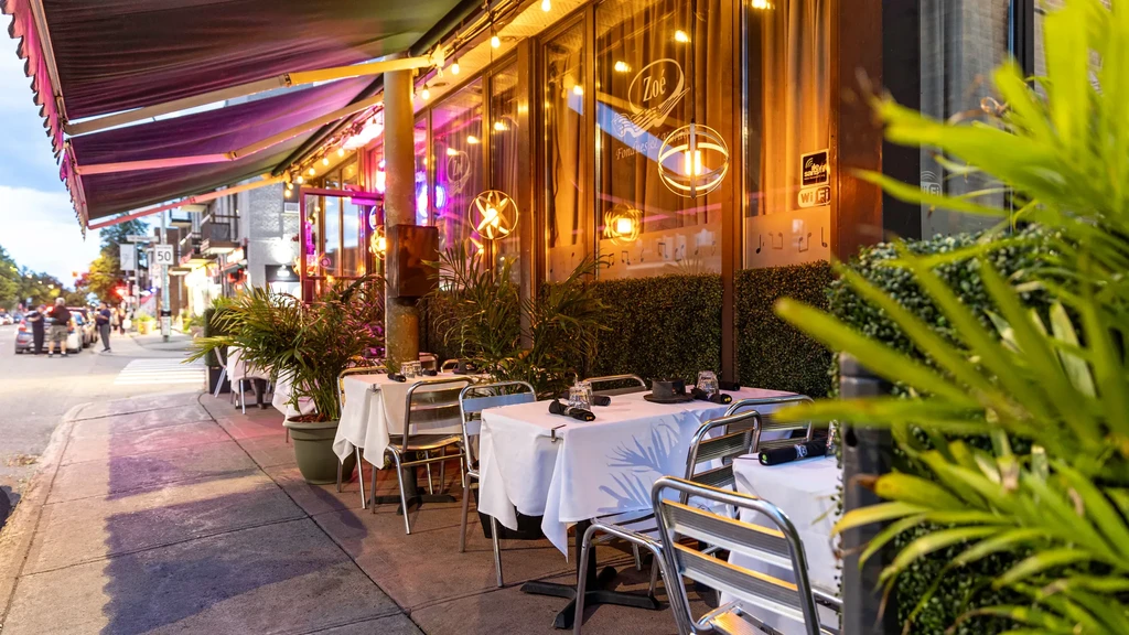 Zoé restaurant exterior at dusk, purple awning, outdoor seating, glowing lights.