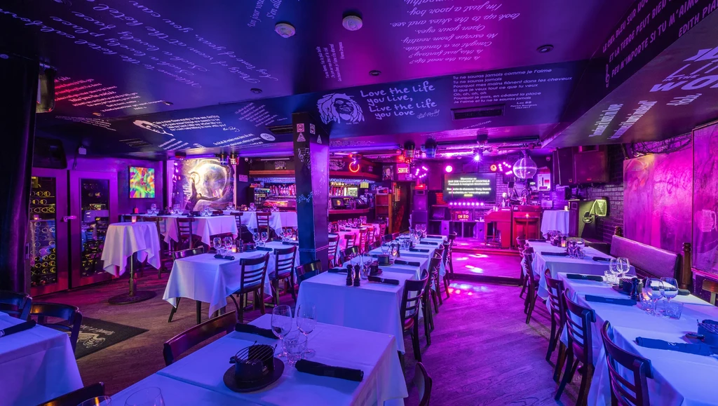 Purple-lit restaurant dining area with script walls, set tables, stage.