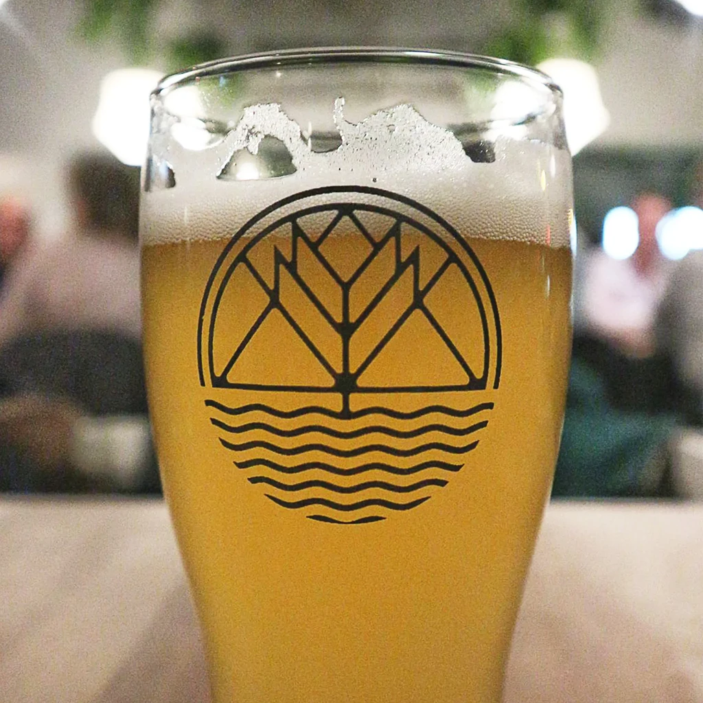 Glass of amber beer with mountain logo and white foam.