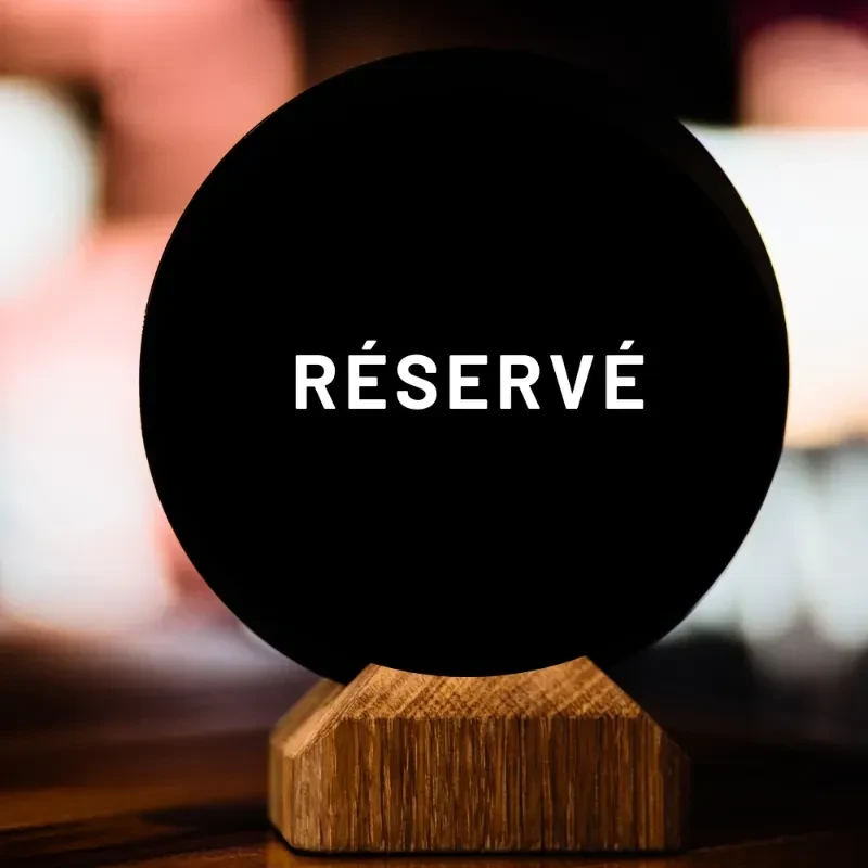 Circular black "RÉSERVÉ" sign on a faceted wooden table base.