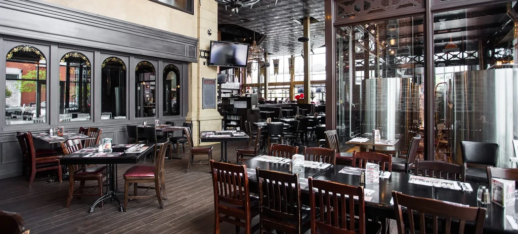 Spacious brewpub interior with dining area, bar, and visible fermentation tanks.