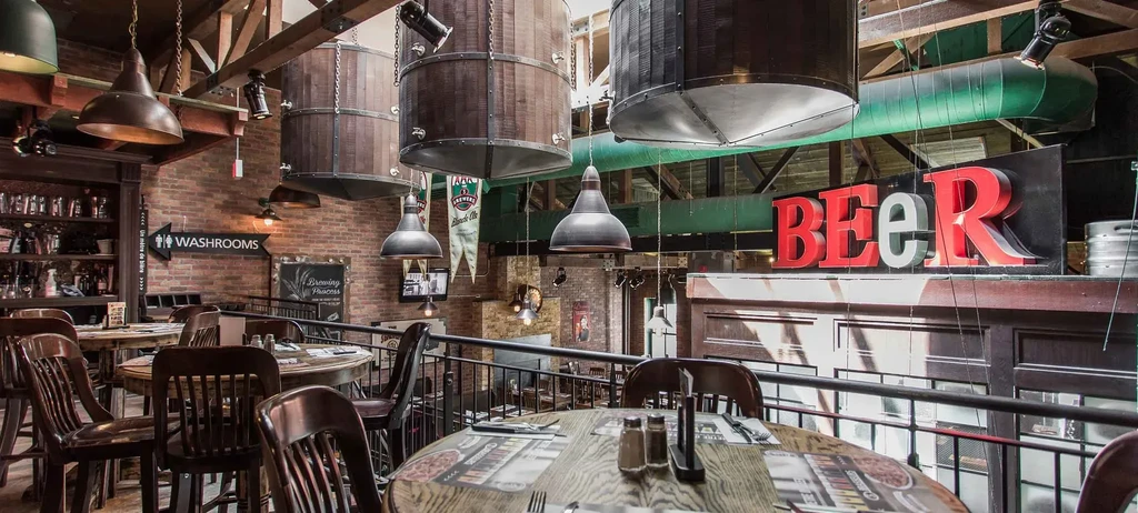 Multi-level industrial-rustic restaurant interior with brick, wood, barrels, and BEER sign.