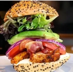 Stacked chicken and bacon sandwich on a seeded bun with fresh vegetables.