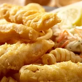 Plate of crispy golden fish and chips, with coleslaw and lemon.