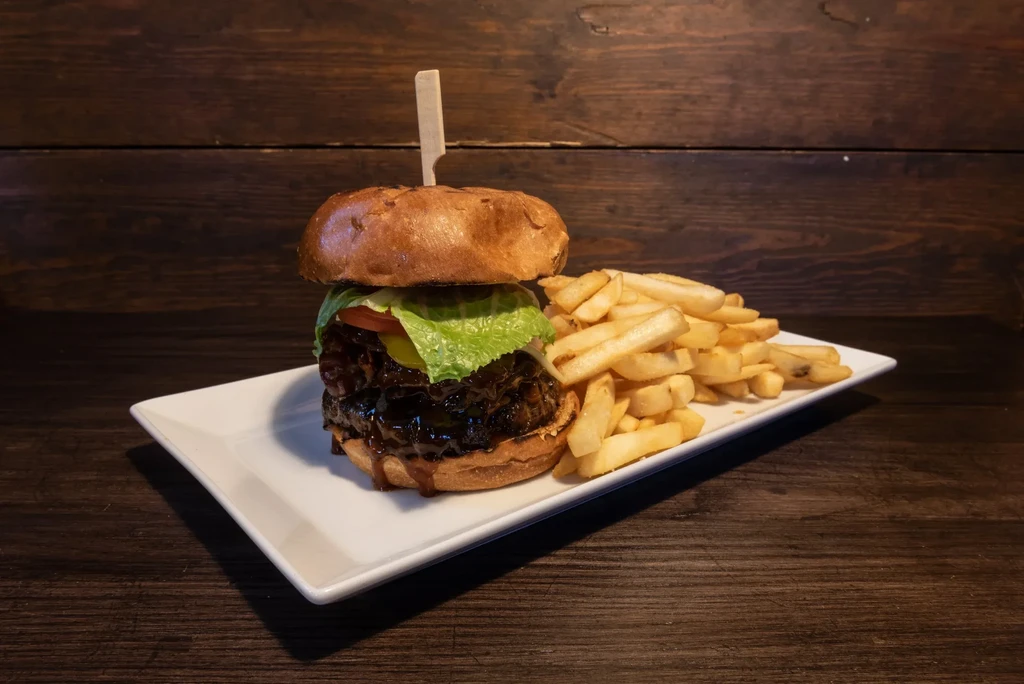 Gourmet double-patty burger, fries, white plate, rustic wooden surface.