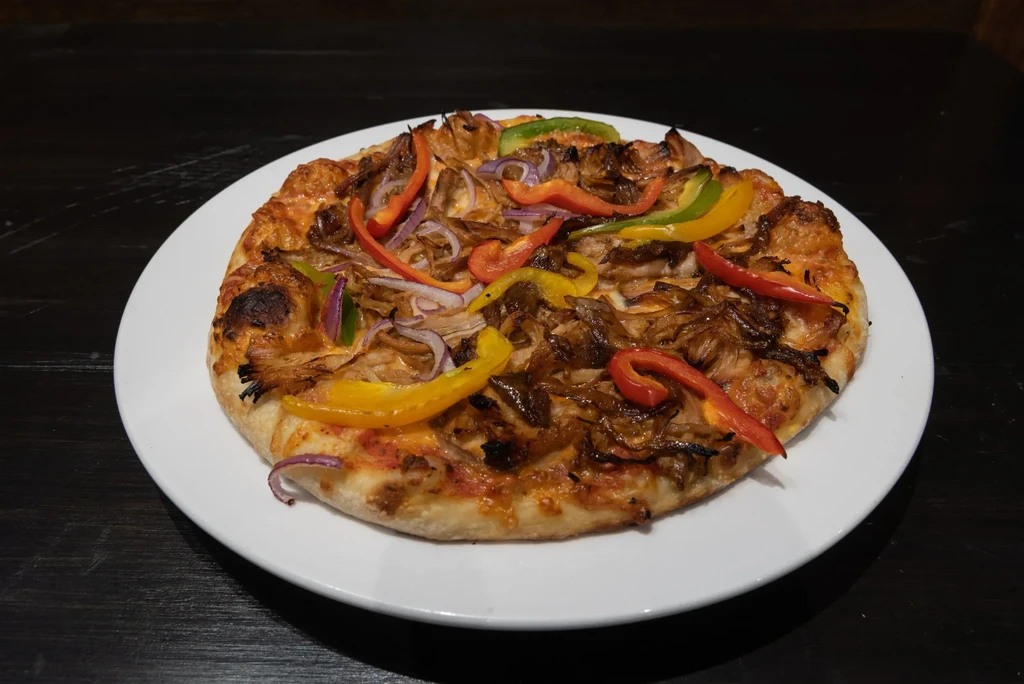Whole pizza with colorful bell peppers, red onion, and dark layer.