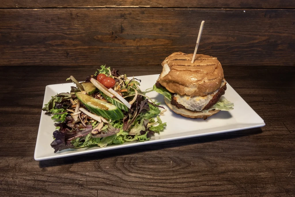 Grilled burger with melted cheese and fresh salad on white plate.