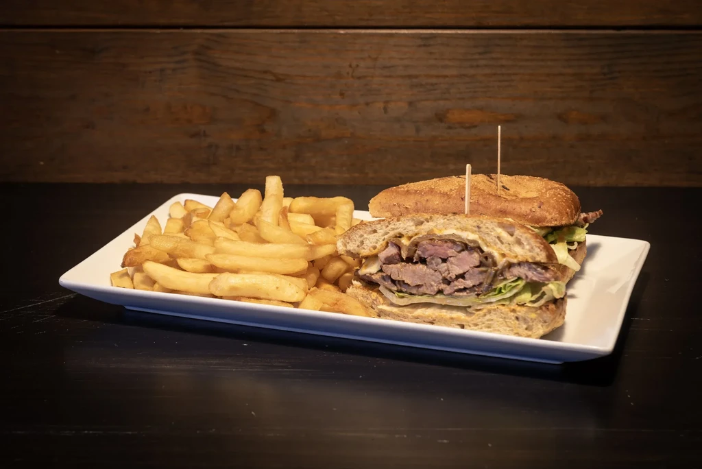 Rustic meat sandwich and golden french fries on a white plate.