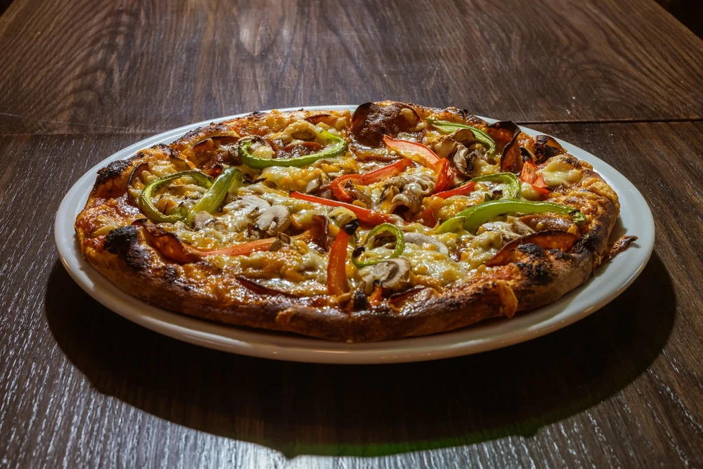 Freshly baked pizza with cheese, peppers, mushrooms on a wooden table.
