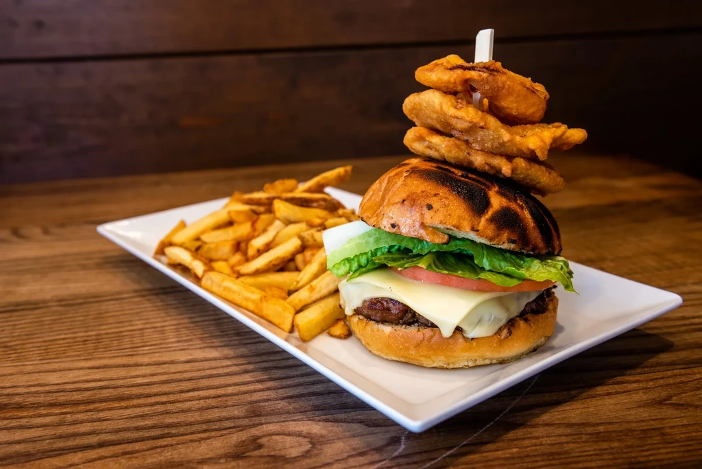 Close-up: Stacked burger with onion rings and golden french fries.